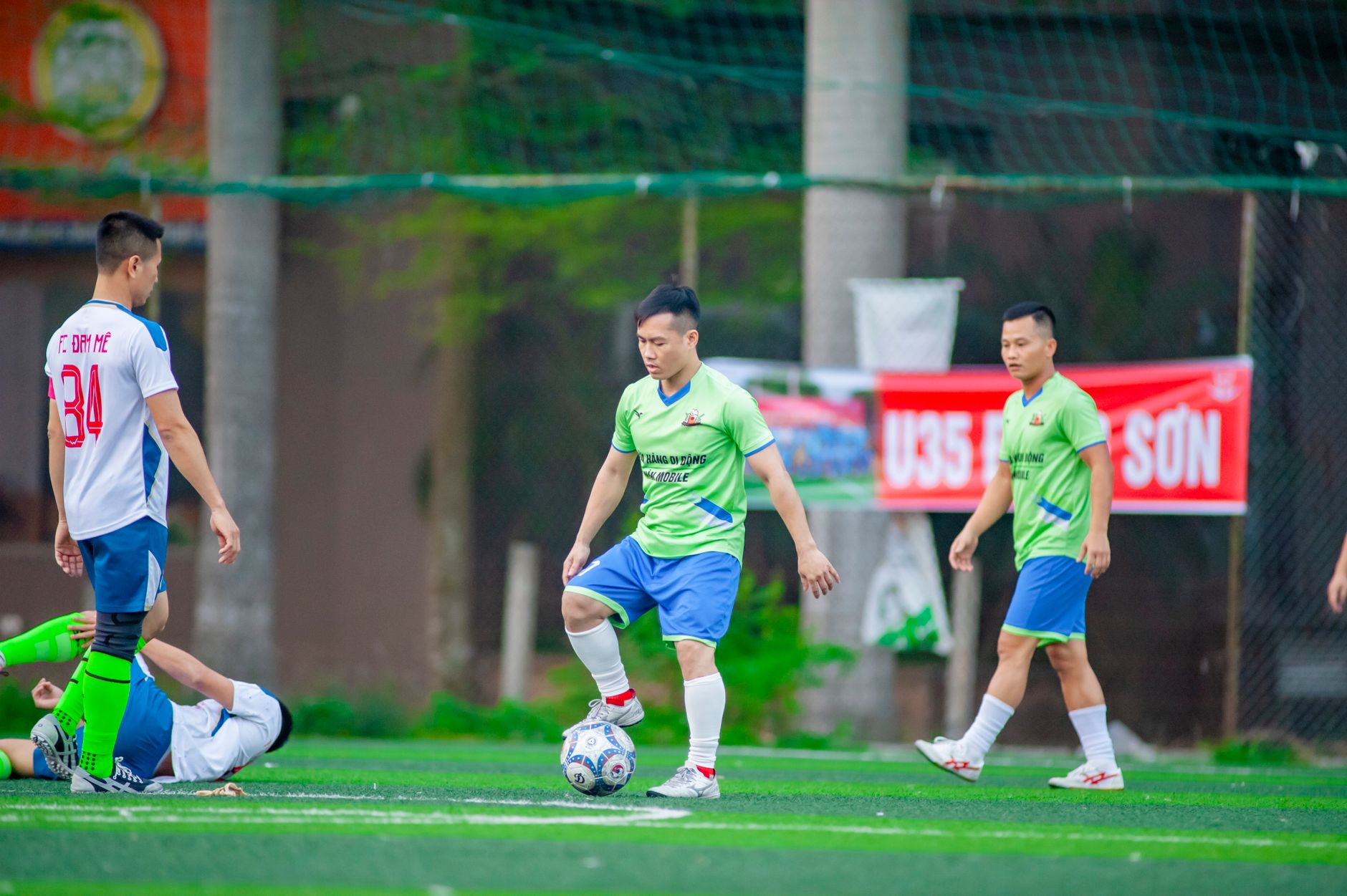 Three football players competing in a small-sided 3v3 game on a compact artificial pitch
