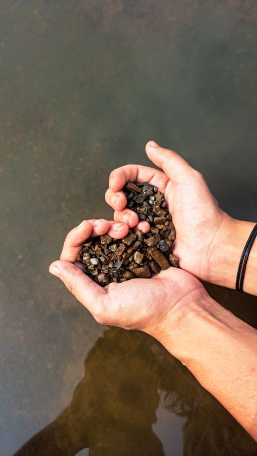 Free Hands forming a heart shape with pebbles over water, symbolizing love and nature. Stock Photo