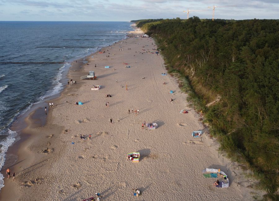 A stunning aerial view of a sandy beach along the Baltic Sea, bordered by lush forests.