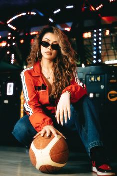 Fashionable woman in an arcade setting holding a basketball.
