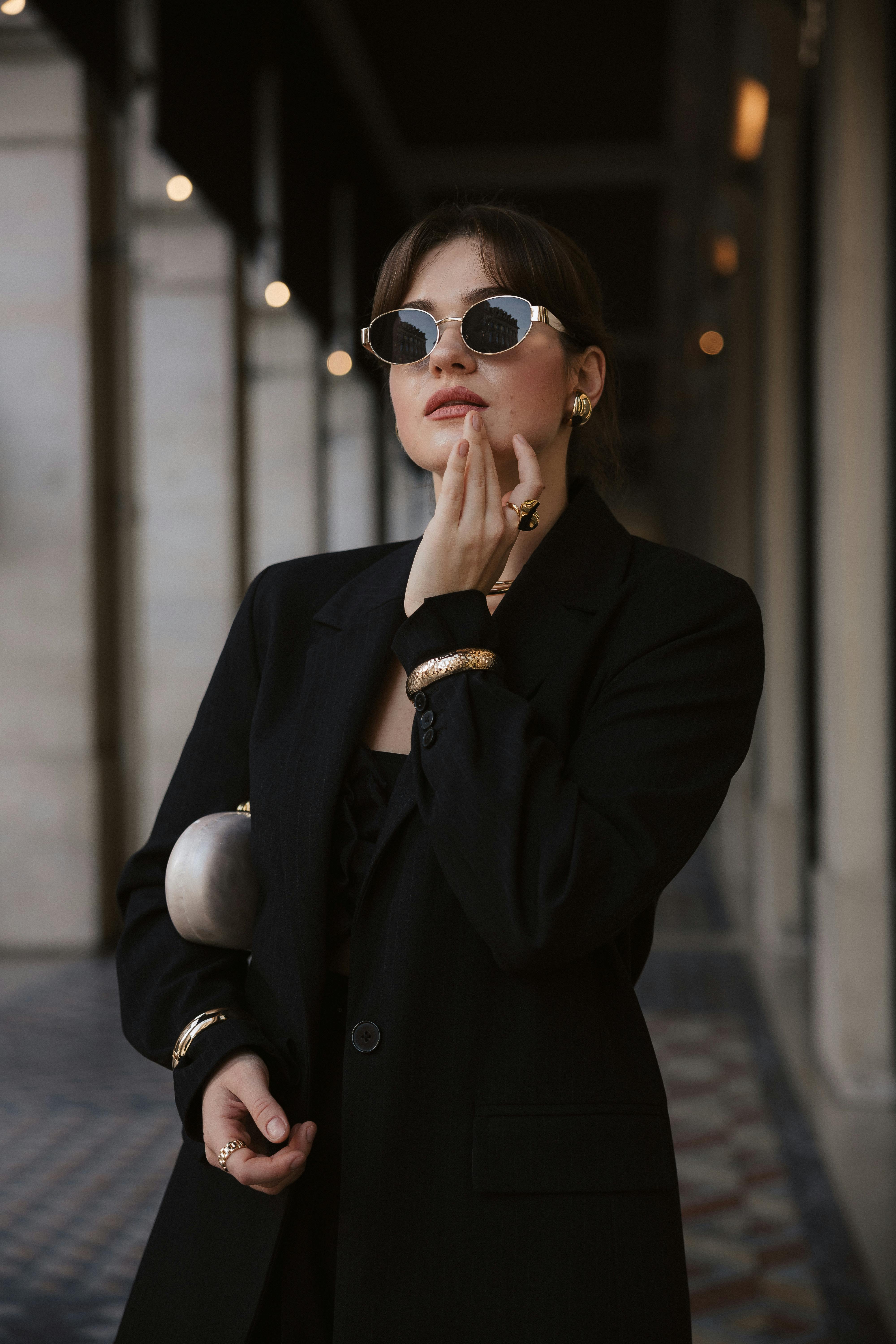 Elegant woman in sunglasses and black attire posing confidently in historic Parisian passageway.