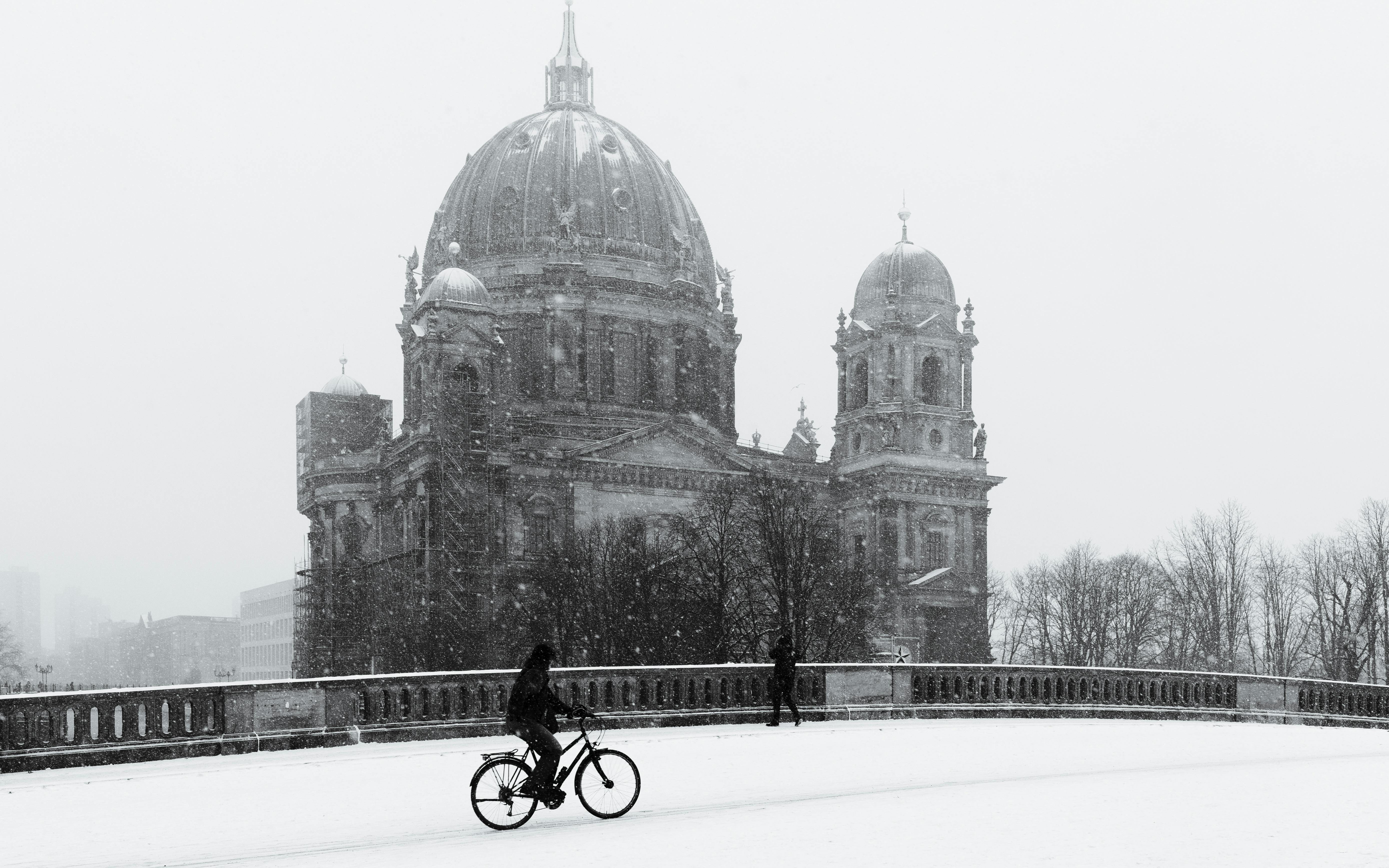 A cyclist in front of Berlin Cathedral during a snowfall, capturing the essence of winter in the city.