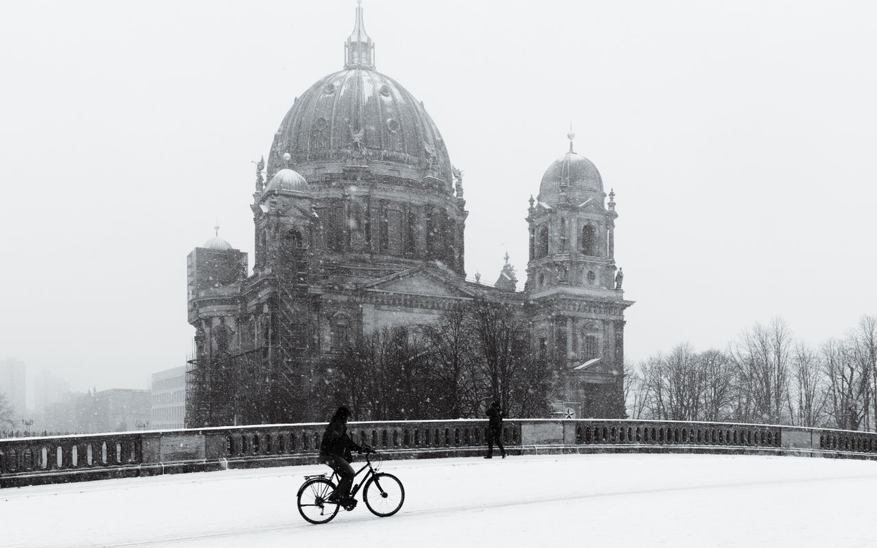 a cyclist in front of berlin cathedral during a snowfall capturing the