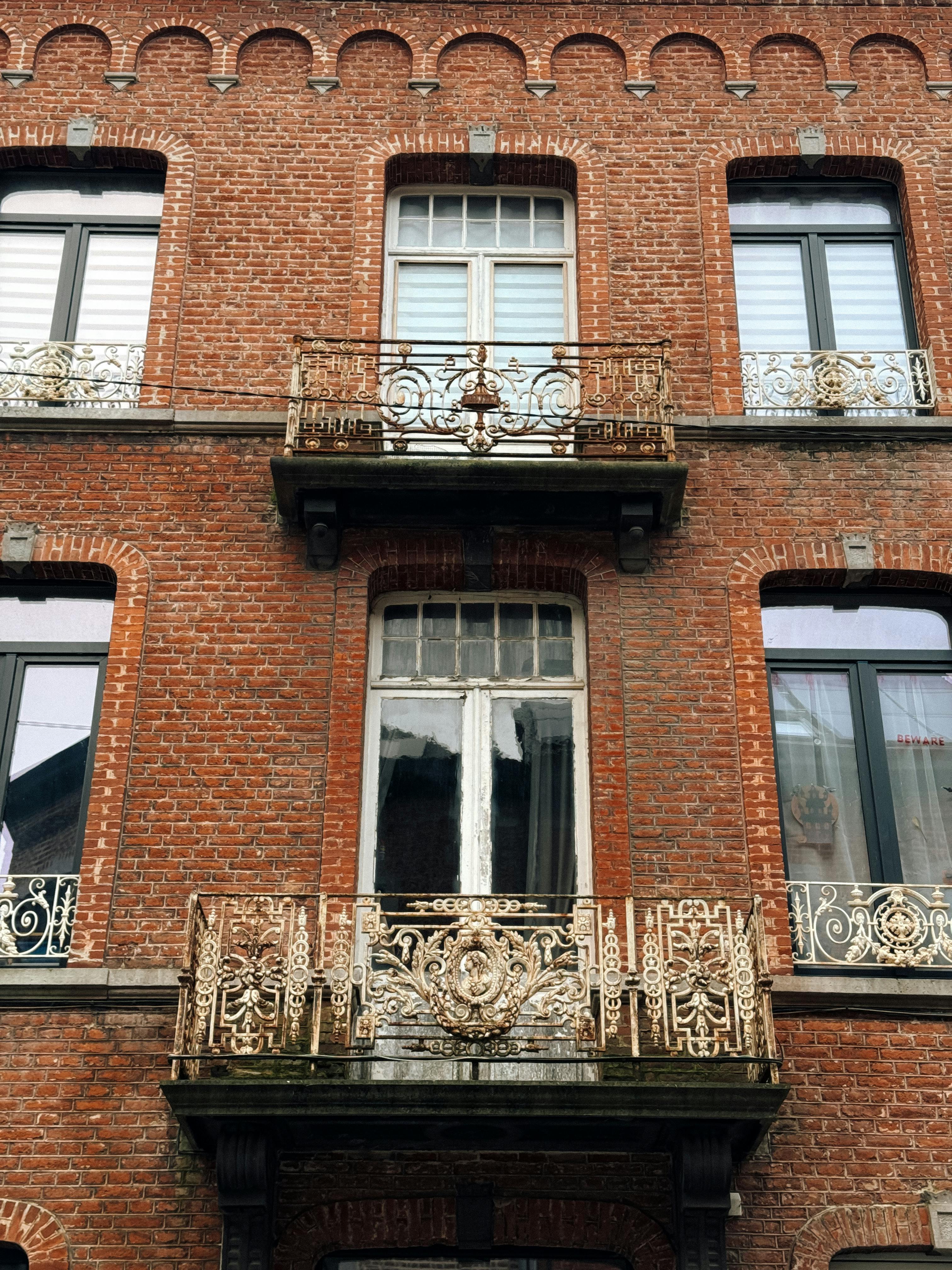 A detailed view of a red brick building facade in Dinant, Belgium, featuring intricate ironwork balconies.
