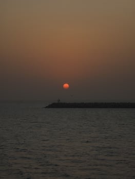 A serene sunset casting orange hues over calm ocean waters, perfect for tranquil moments.