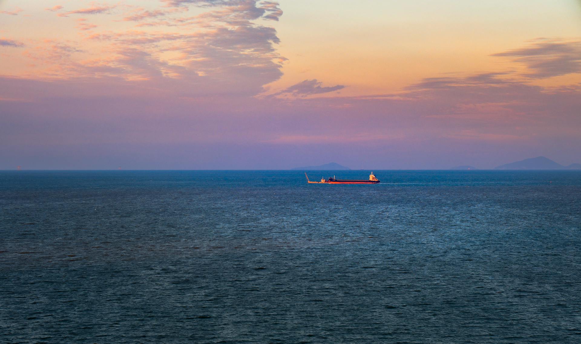 A cargo ship sails under a vibrant sunset over the ocean, creating a serene maritime scene.