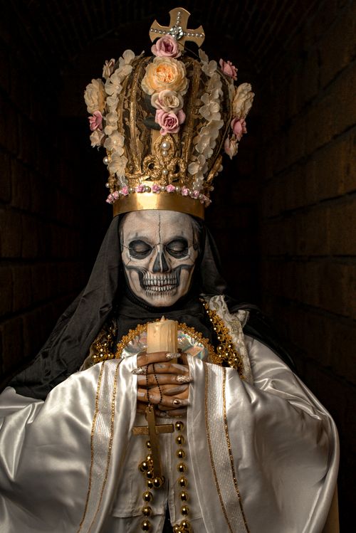 Free Gothic figure with skull face and ornate floral crown, holding a candle in a dimly lit setting. Stock Photo