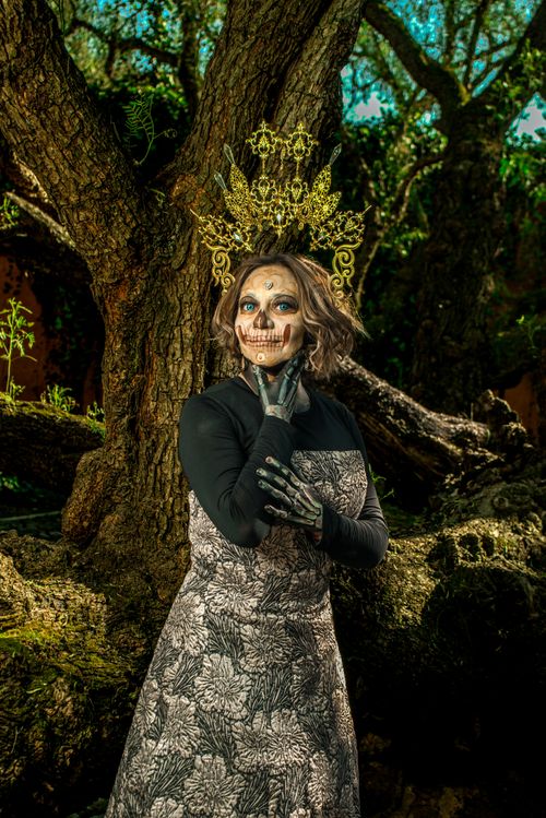 Free A woman with skull makeup and an ornate crown poses in a mystical forest. Stock Photo