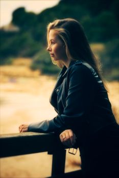 A woman in a leather jacket gazes thoughtfully outdoors, creating a serene mood.