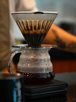 Close-up of coffee brewing in a glass pour-over device on a scale in a cozy café.