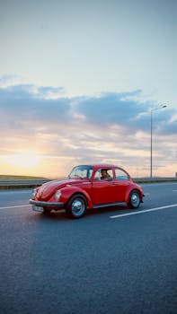 Retro red Volkswagen Beetle driving on a highway at sunset, capturing nostalgia and freedom.