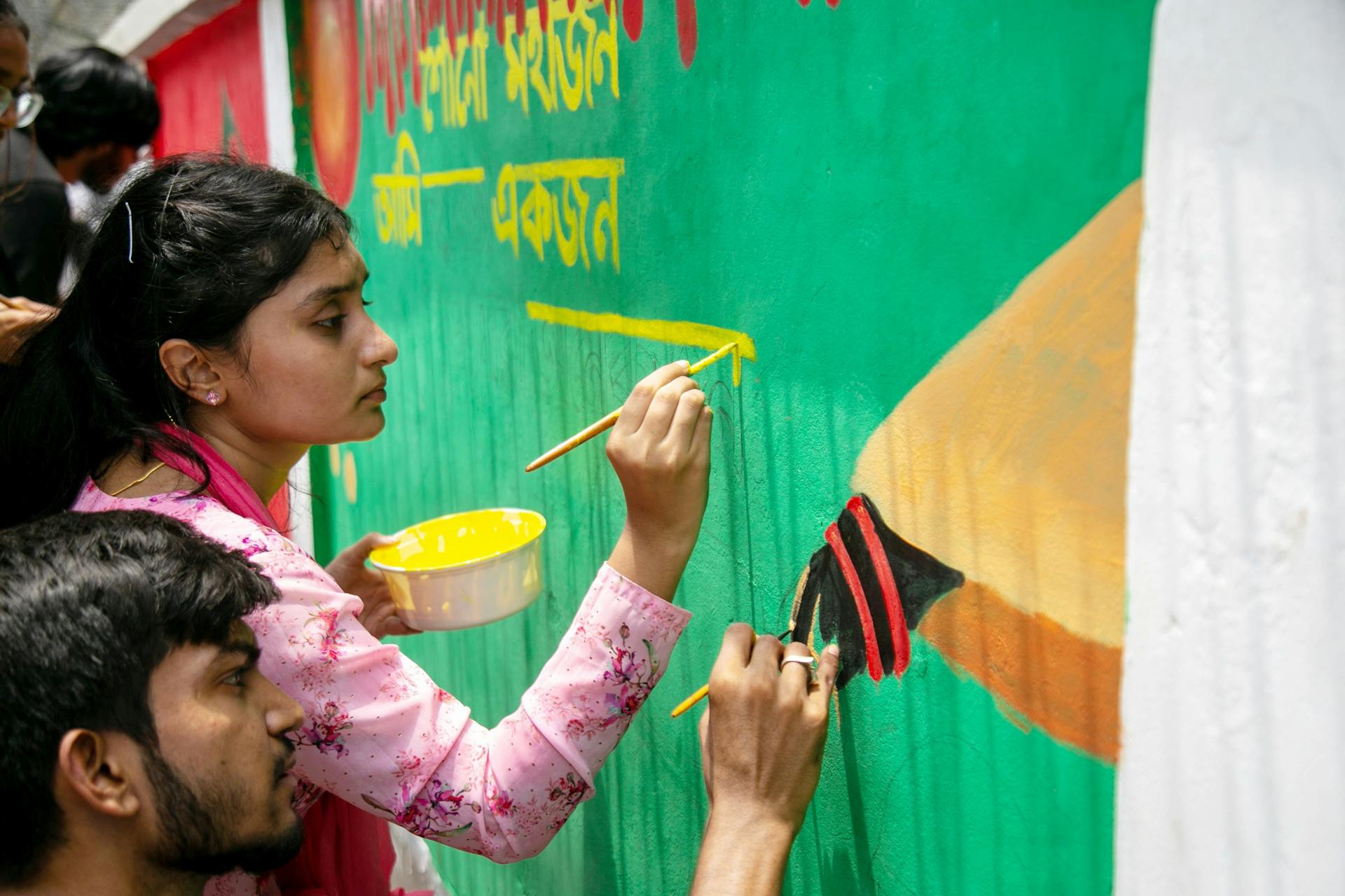 Young adults painting a colorful mural on an outdoor wall, showcasing community art.