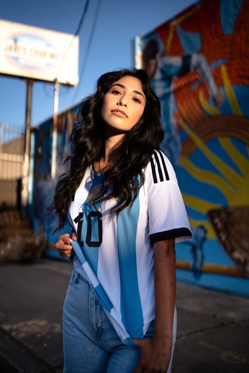 Free Confident woman in an Argentina soccer jersey poses by a vibrant mural outdoors. Stock Photo