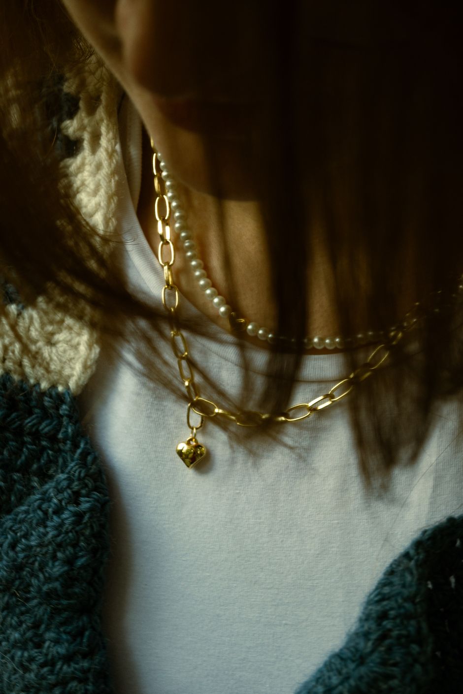 Layered gold and pearl necklaces worn with a knit sweater
