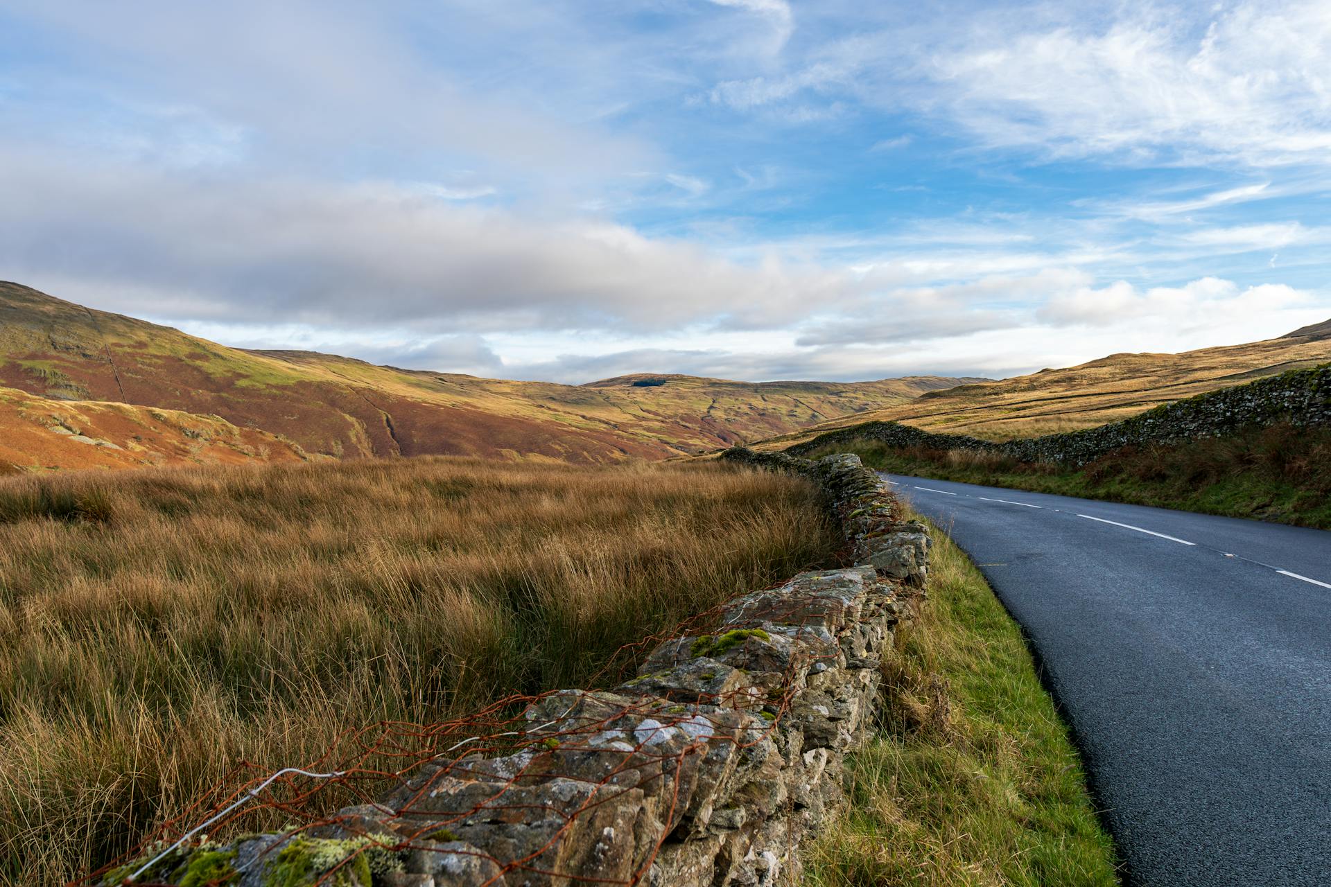 Beautiful winding road through a picturesque countryside landscape with stone walls under a clear sky.