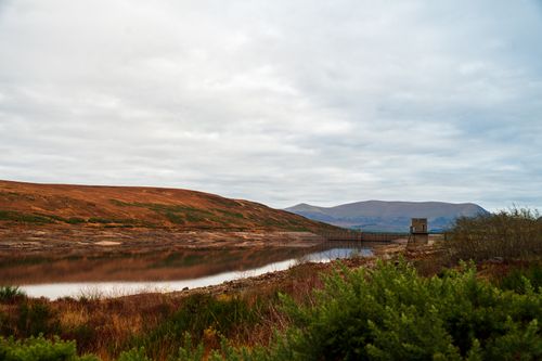 Free Tranquil landscape of a lake with rolling hills and a cloudy sky. Ideal for nature themes. Stock Photo