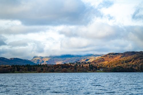 Free Beautiful autumn landscape featuring a lake with colorful mountains and cloudy sky. Stock Photo