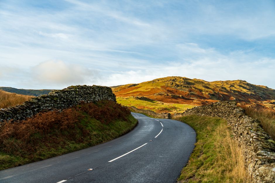 Beautiful winding road with stone walls through vibrant countryside and hills. Perfect for travel and nature enthusiasts.
