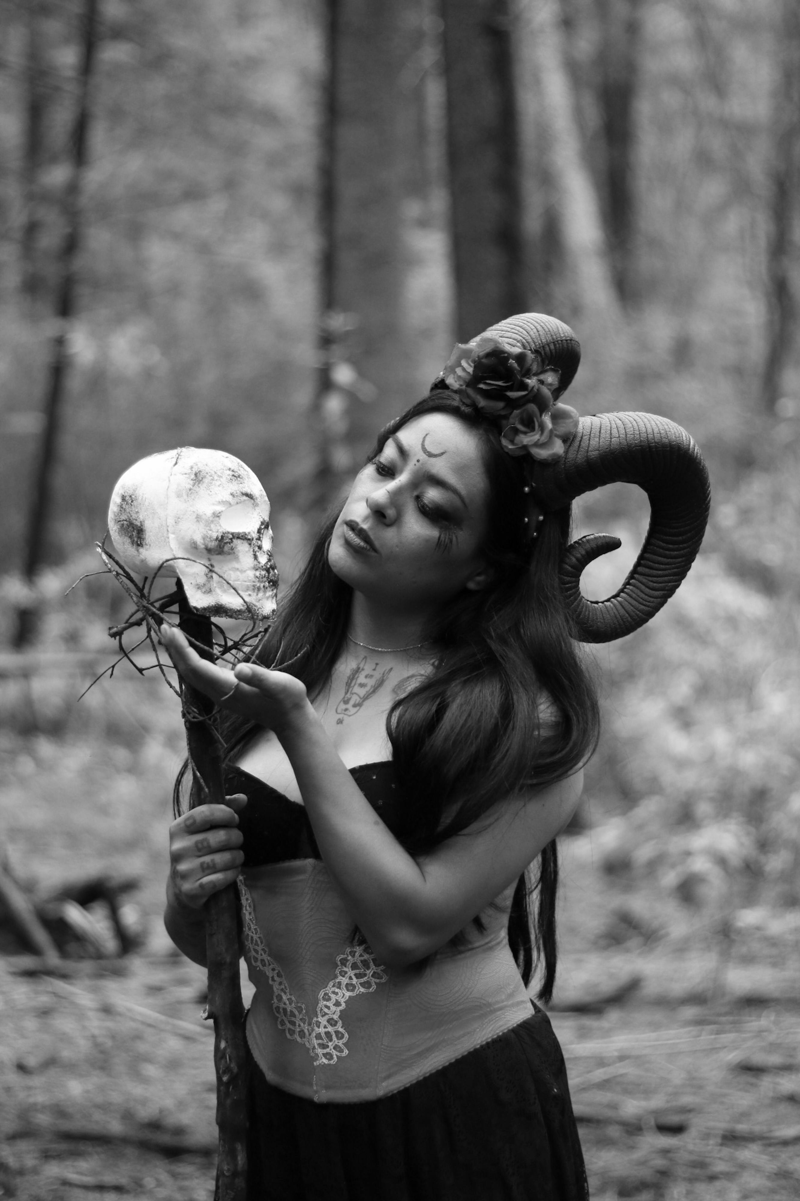 Gratuit Une femme mystique avec des cornes de bélier tenant un crâne dans une forêt, créant une atmosphère fantastique étrange. Photos