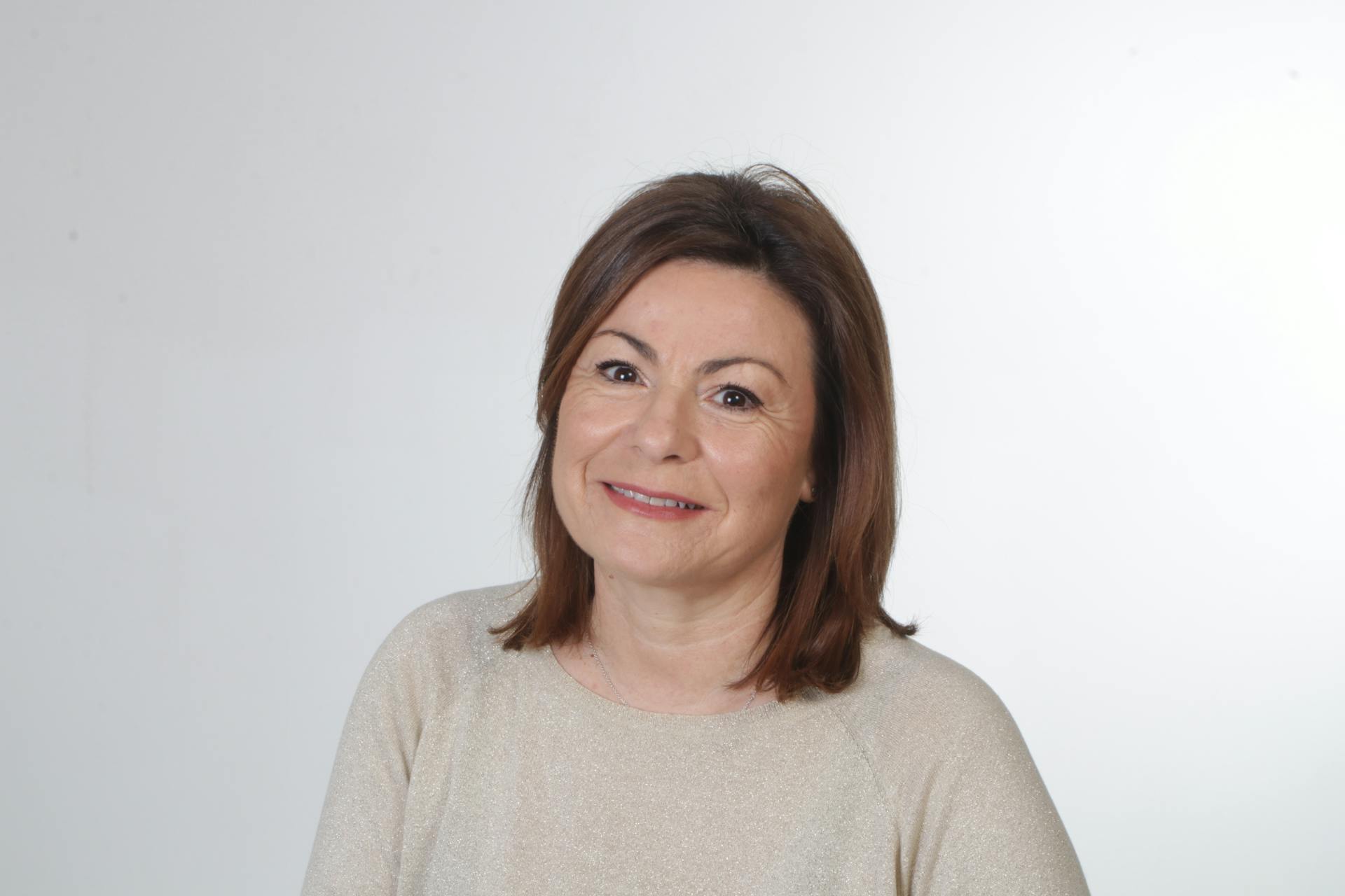 Portrait of a smiling middle-aged woman with brown hair against a neutral background.