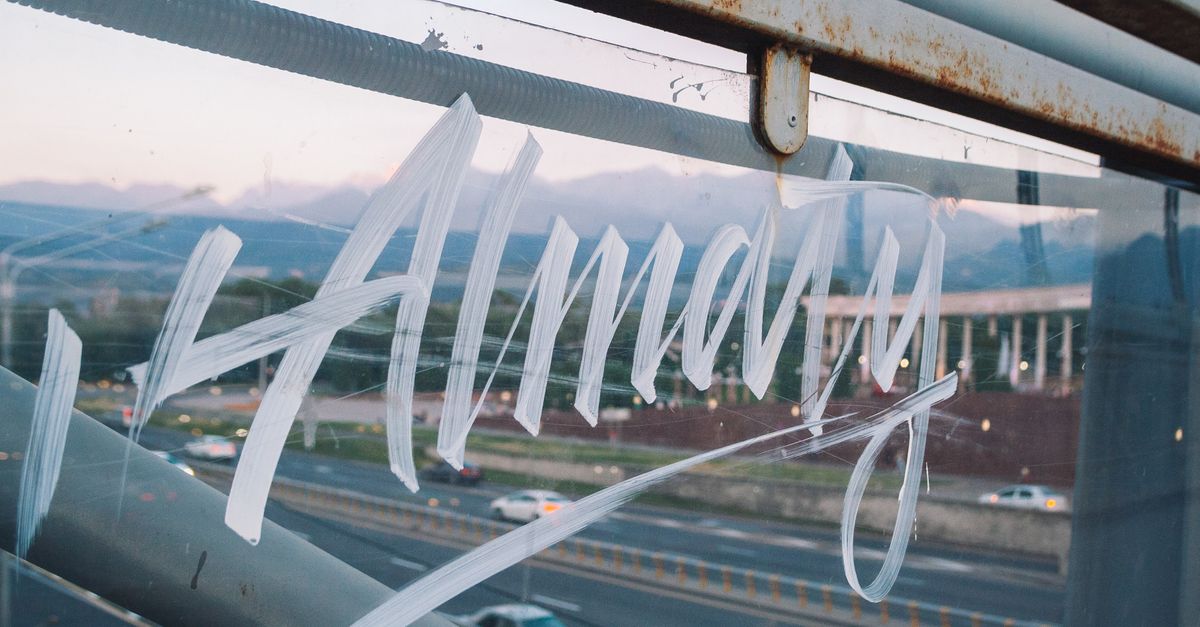 Artistic graffiti of Almaty on glass overlooking a cityscape with mountains.