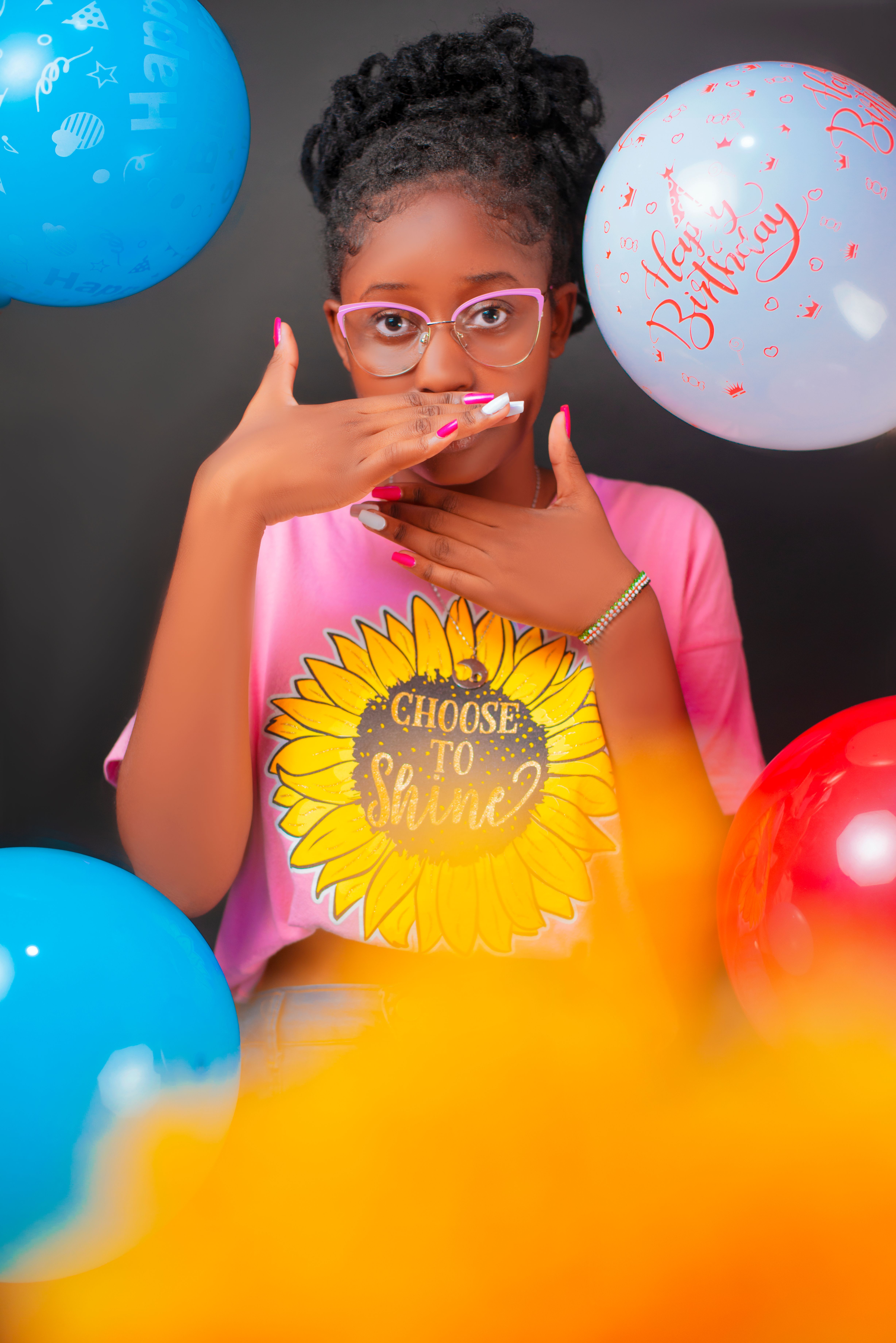 Colorful birthday celebration with young woman and balloons wearing 'Choose to Shine' t-shirt.