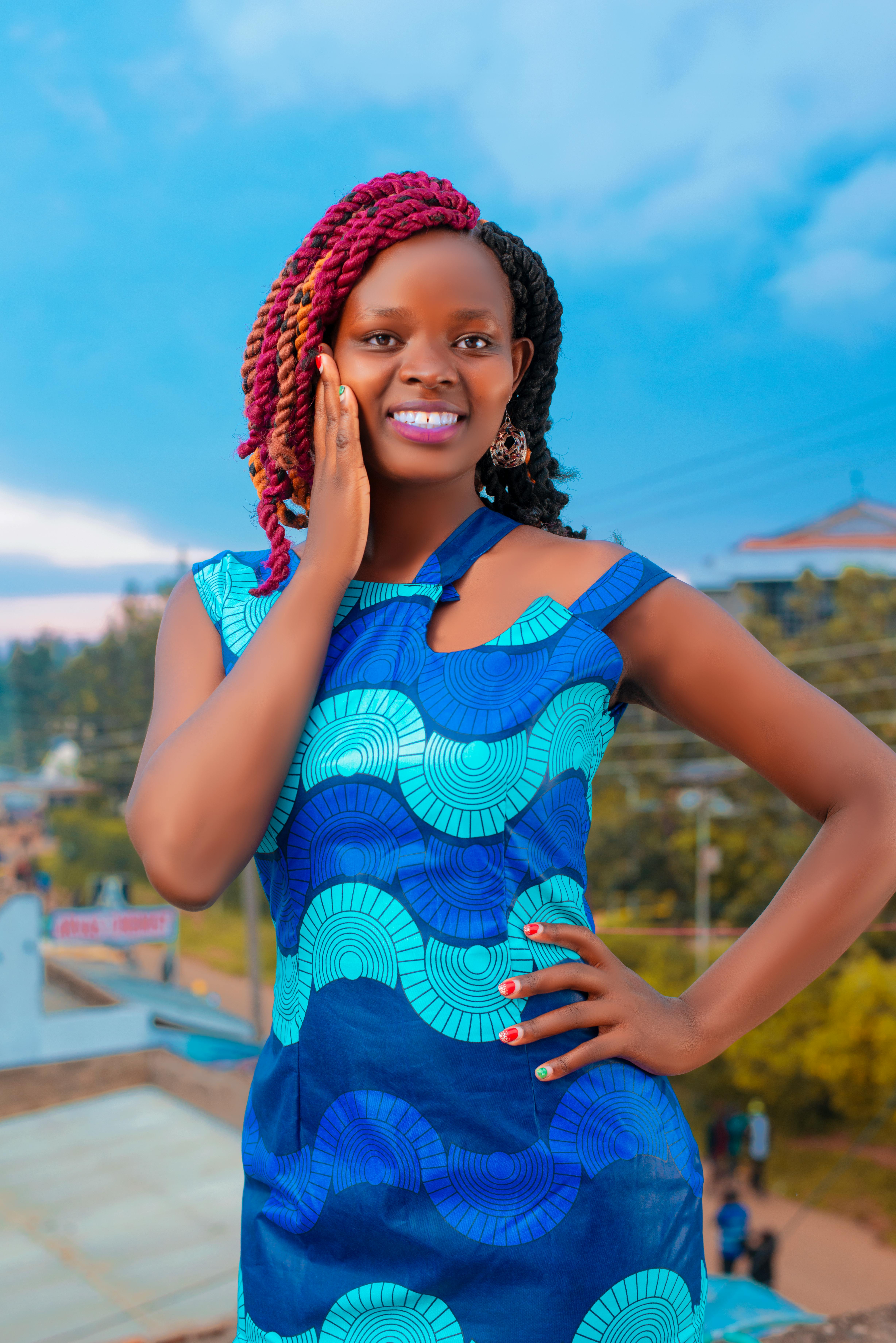 A cheerful woman poses with a smile in a vibrant blue dress against an urban backdrop.