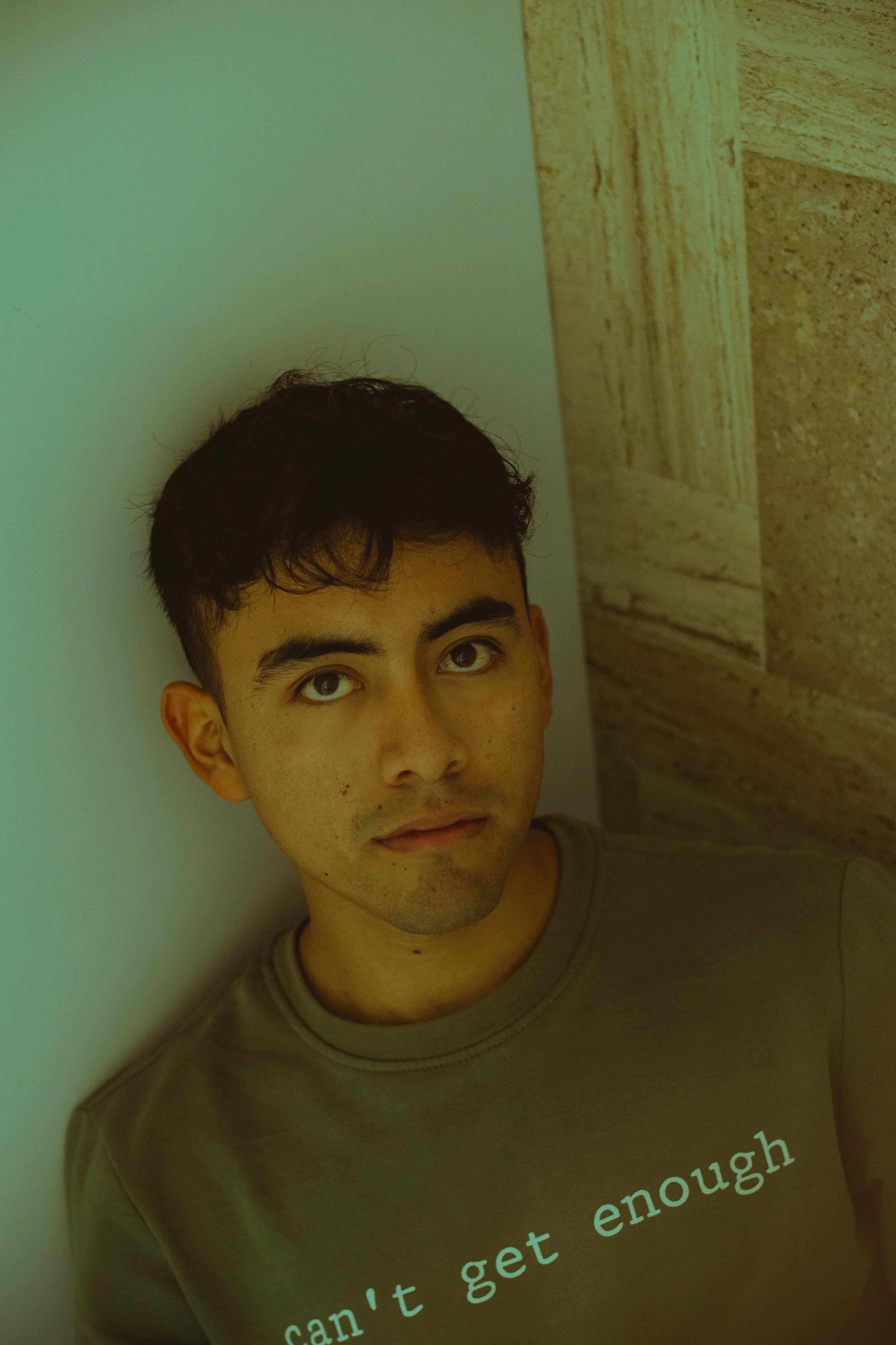 Portrait of a young man with contemplative look against a wall inside.