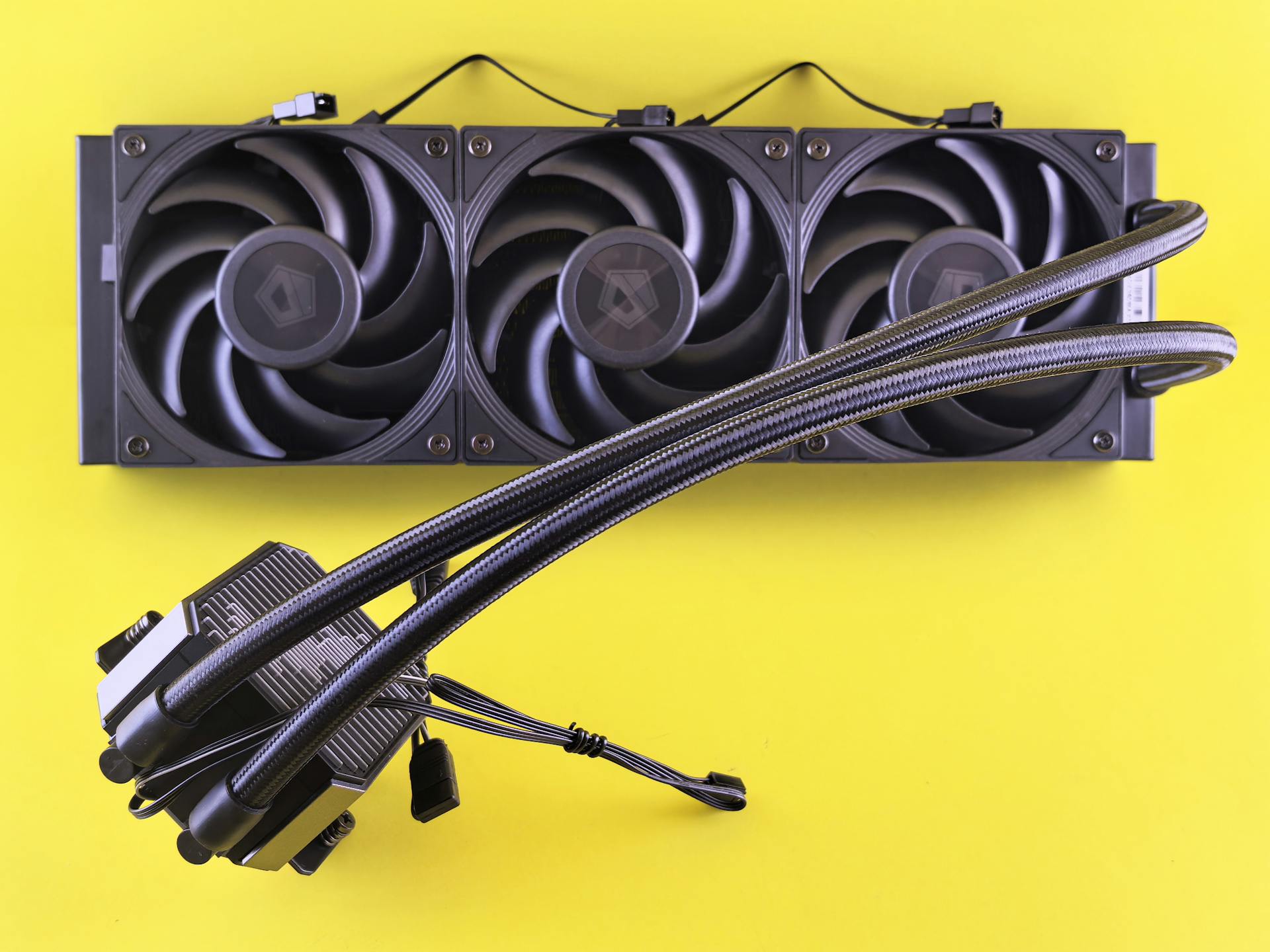 A close-up of a computer cooling system with three fans on a vibrant yellow background.