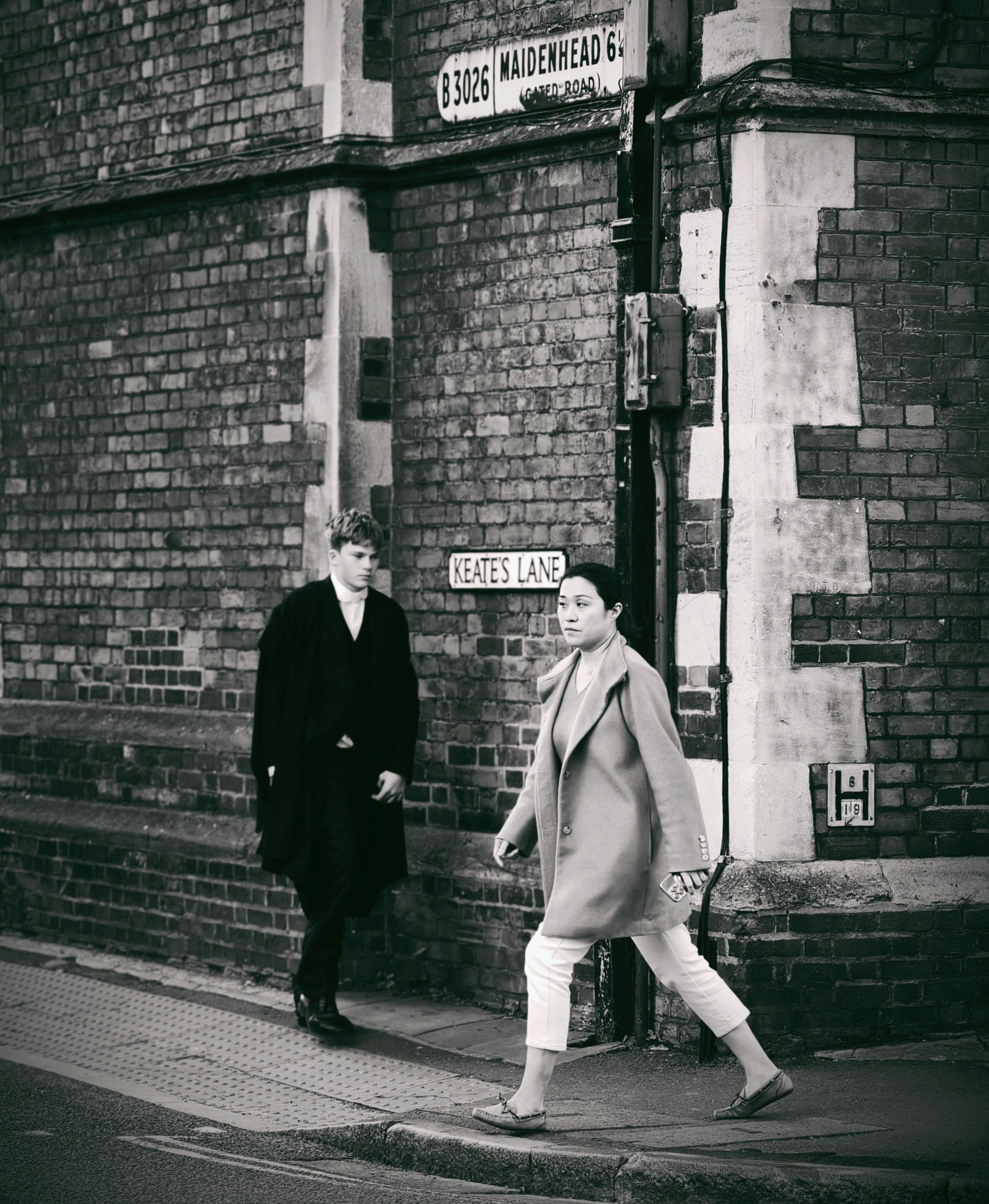 Black and white photo of two adults in coats walking on Keates Lane.