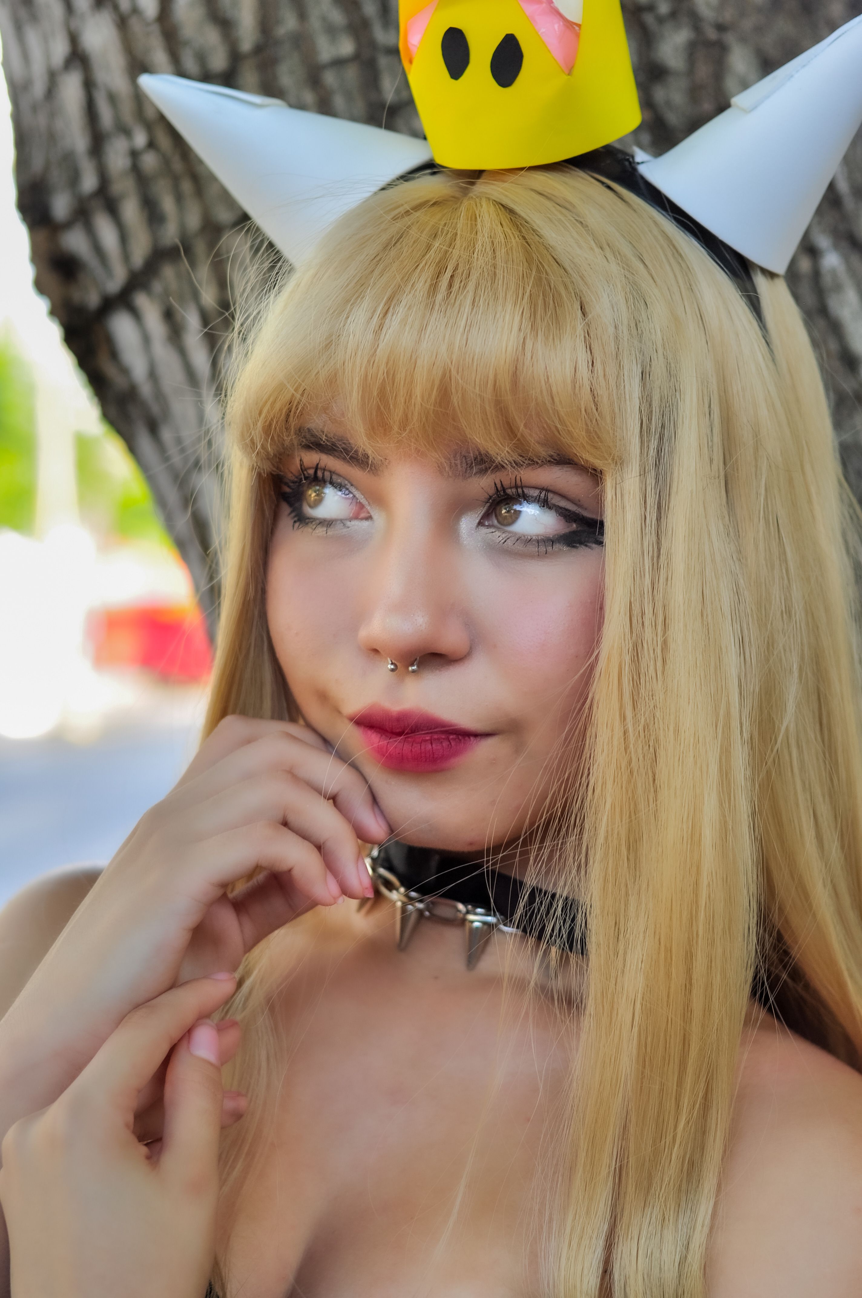 Blonde cosplayer with crown, horns, and septum piercing posing outdoors. Vibrant portrait.