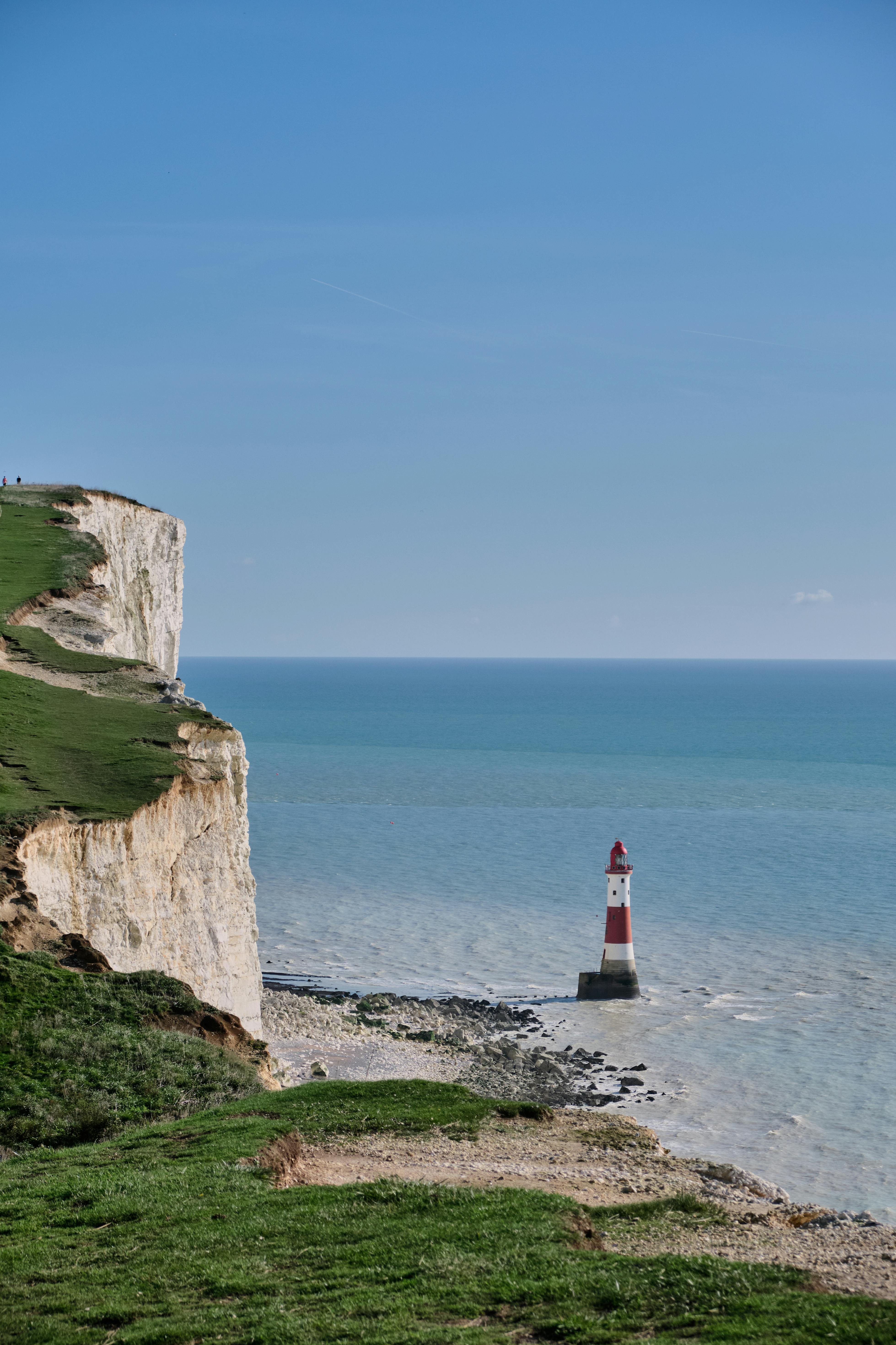 在清澈的蓝天下，白色的悬崖和海洋构成了海滩头灯塔的全景