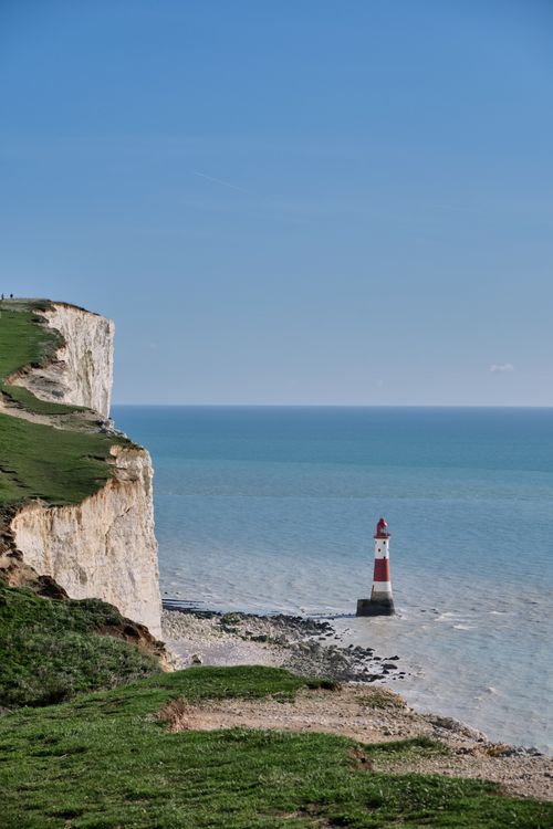 Free Panoramic view of Beachy Head Lighthouse with white cliffs and ocean under clear blue sky. Stock Photo