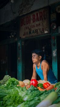 Man stands behind vegetable stall at Jakarta market, colorful produce displayed.