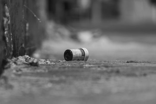 Black and white image of a discarded pill bottle on a gritty city street, capturing urban decay.