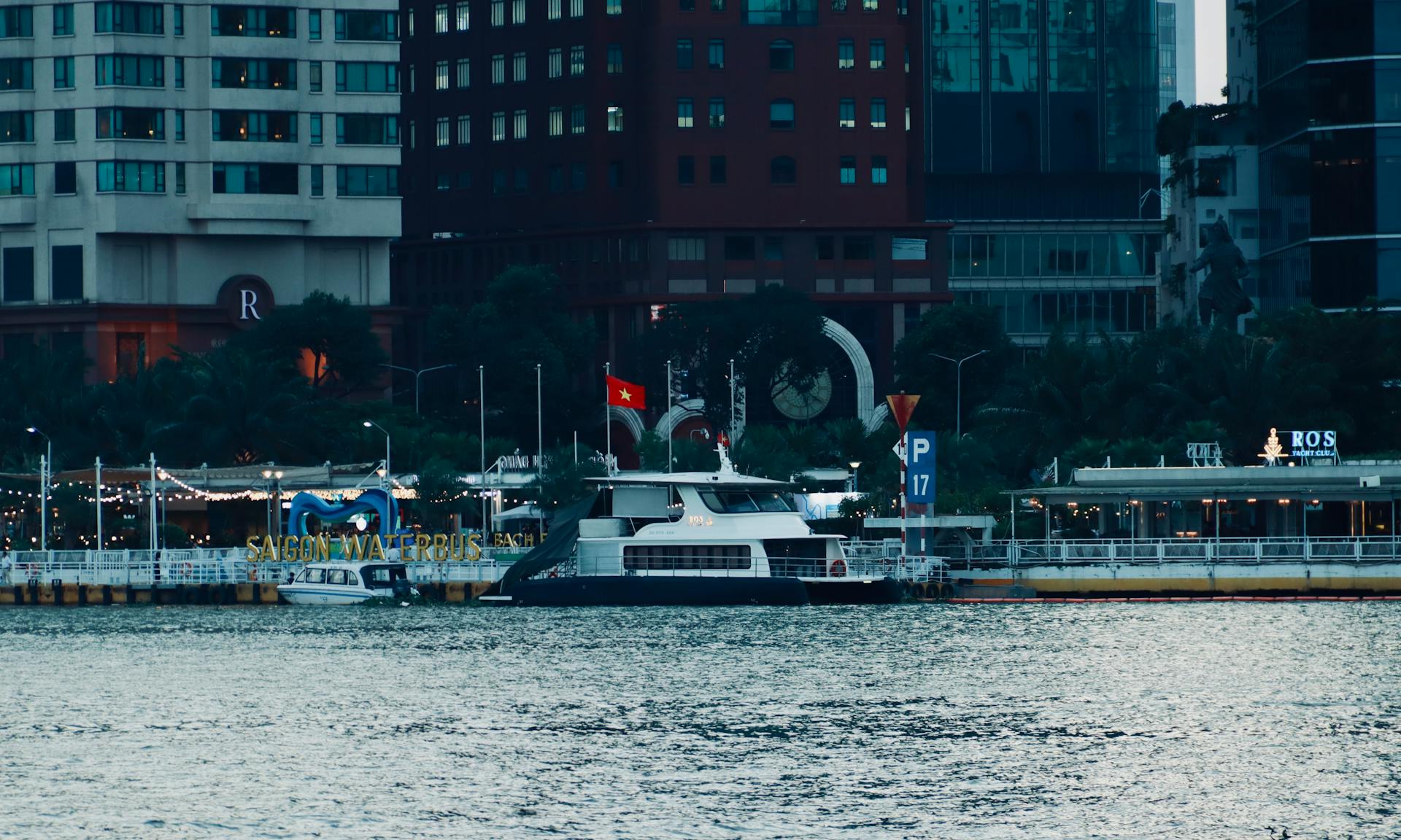 A modern cityscape of Saigon with a docked waterbus on a calm river.