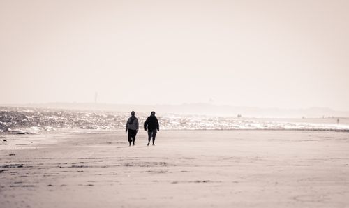 Free Two people walking along a serene beach at sunrise, capturing a calm and tranquil moment. Stock Photo