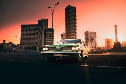Classic vintage car against a city skyline during a vibrant sunset.
