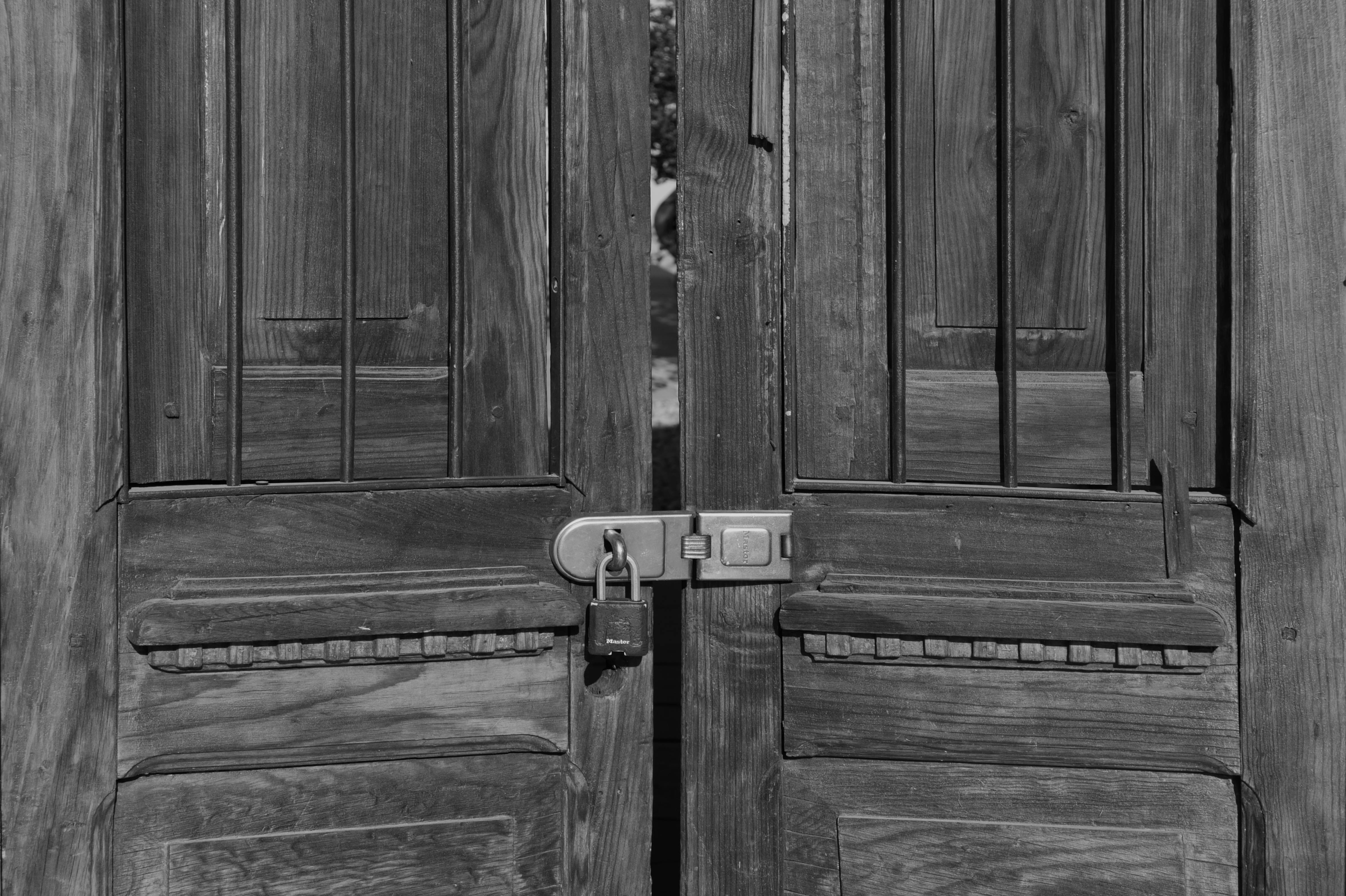 A rustic black and white image of a secured wooden door with a padlock in Ranchos de Taos.