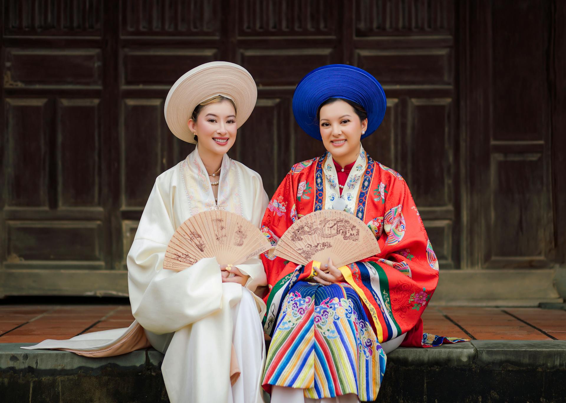 Two women in traditional Ao Dai attire, holding fans in Vietnam.