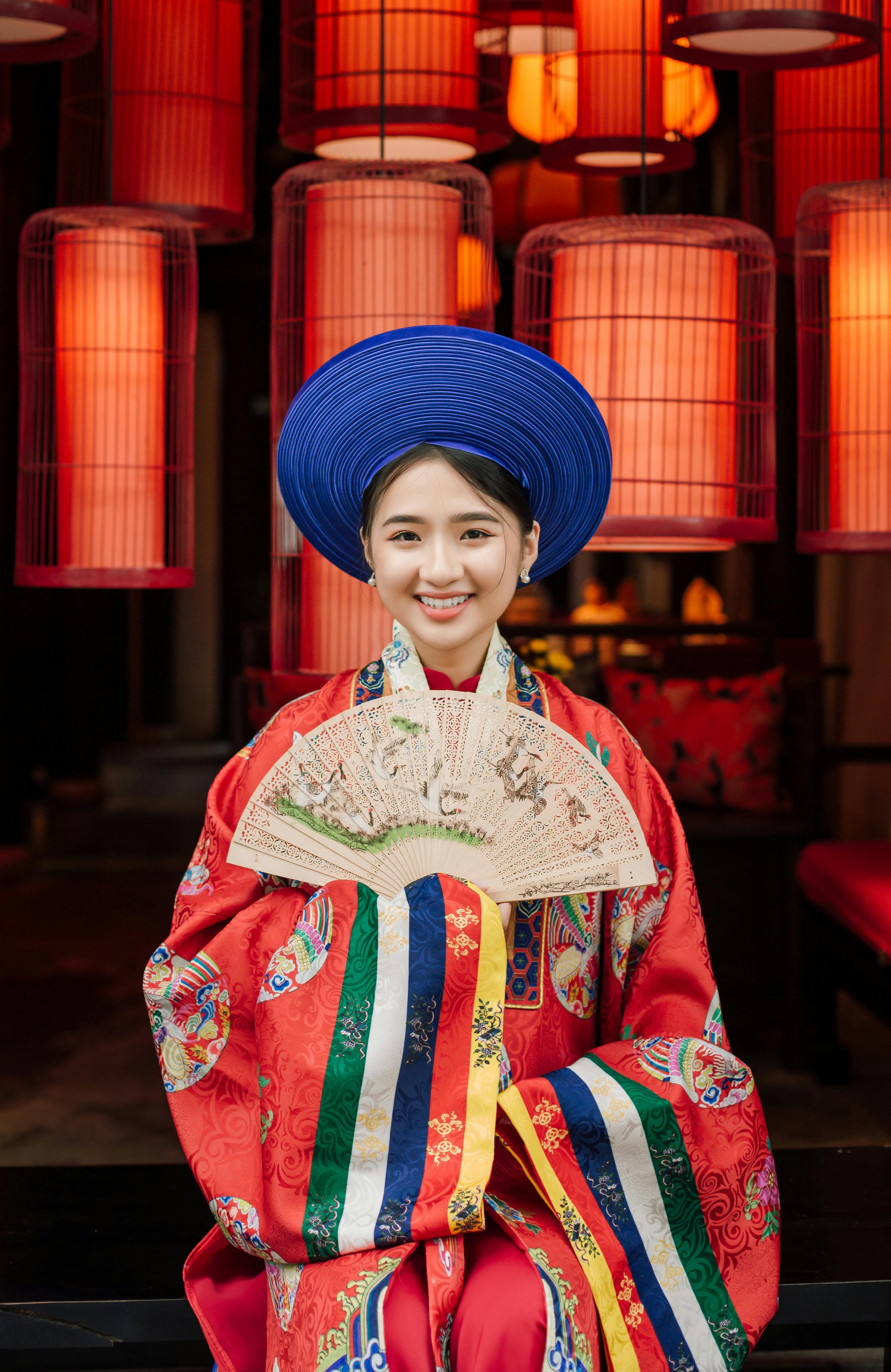 Smiling woman in Vietnamese attire with lanterns backdrop, indoors.