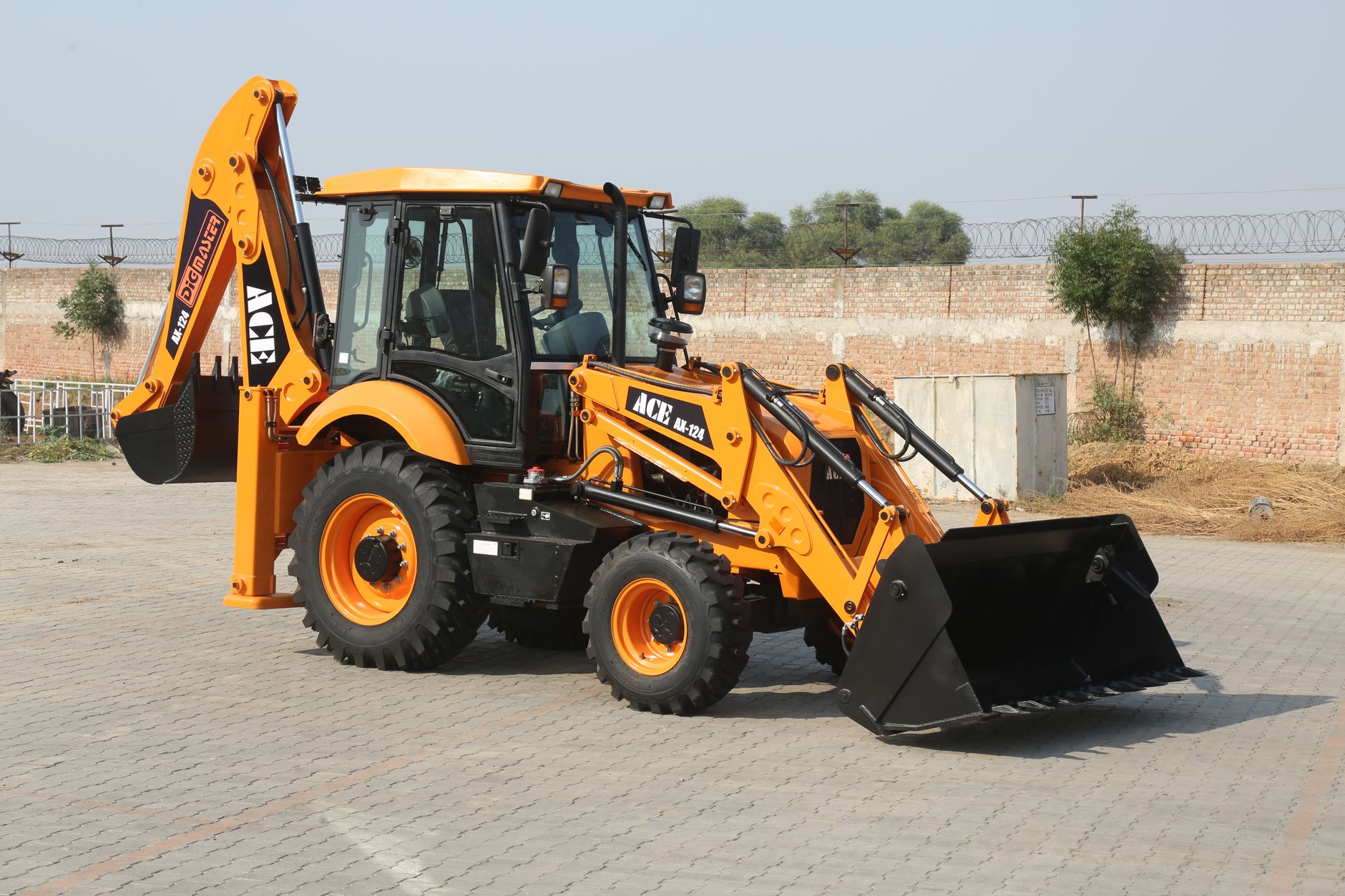 A vibrant ACE AX-124 backhoe loader parked in an industrial yard on a sunny day.