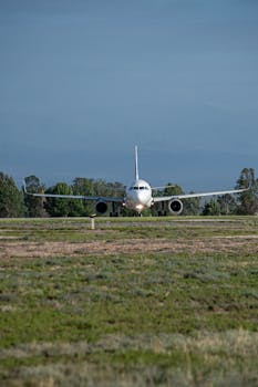 A commercial airplane on a runway amidst lush greenery and distant mountains, ready for takeoff.