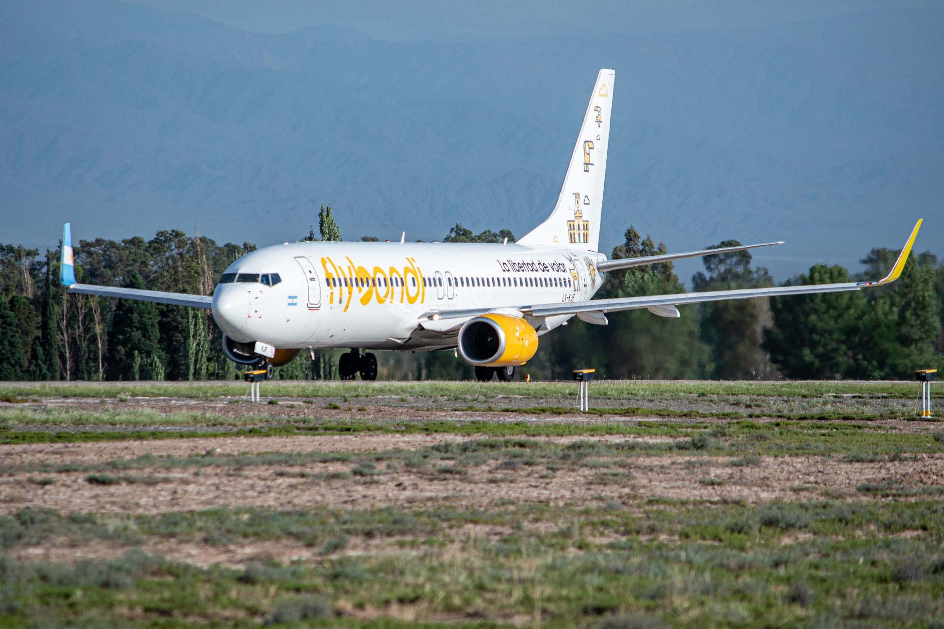 A Flybondi aircraft taxiing on a runway with scenic mountains in the background.