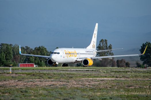 A commercial airliner on the runway surrounded by greenery and mountains.
