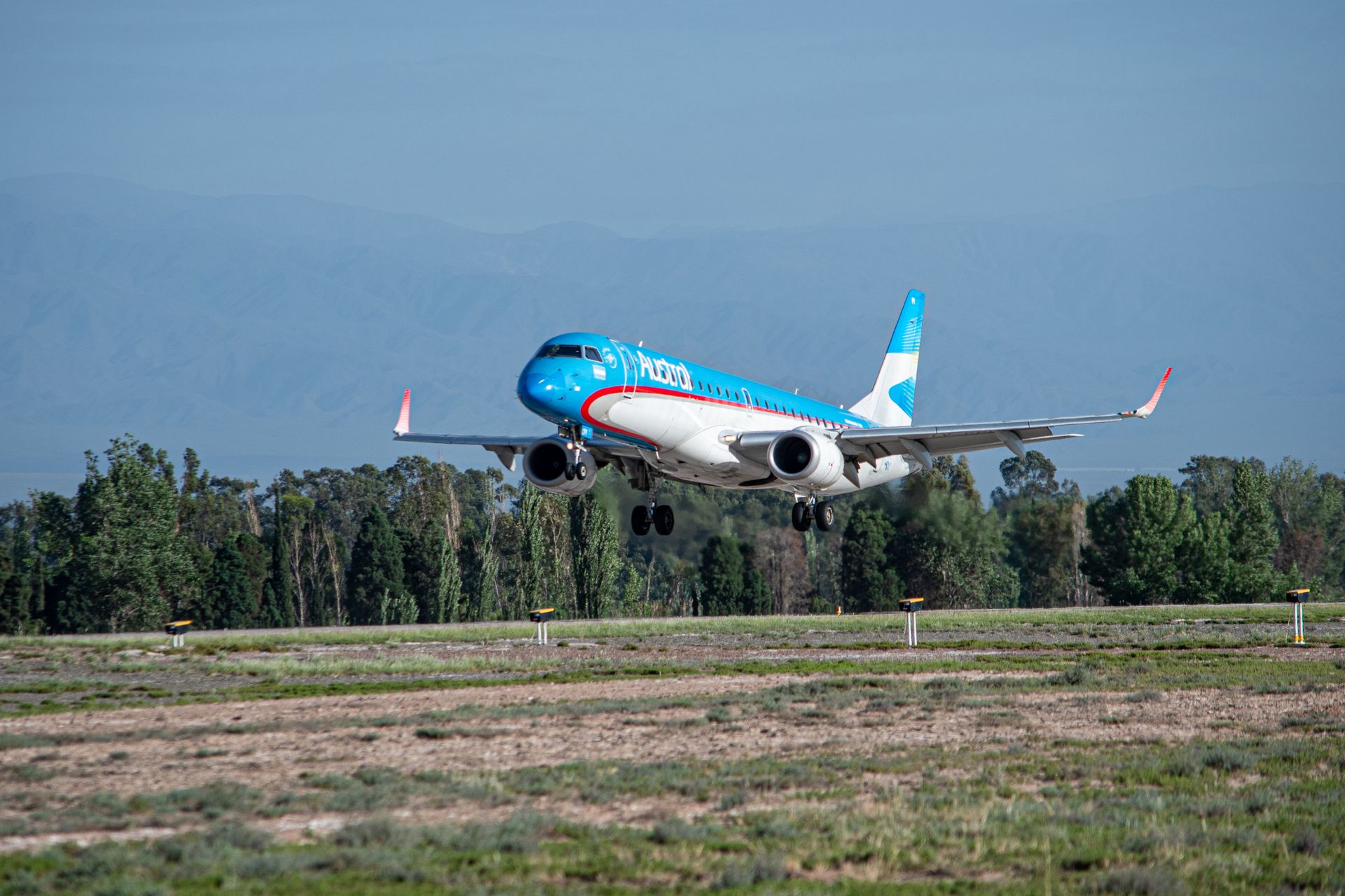 A commercial airplane making a smooth landing on a runway surrounded by greenery and mountains.