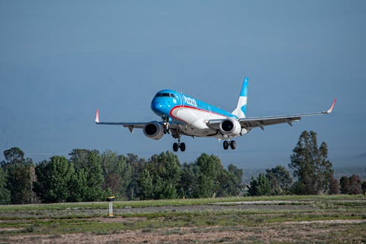 A commercial airplane with blue and white livery approaches landing at an airport runway on a clear day.