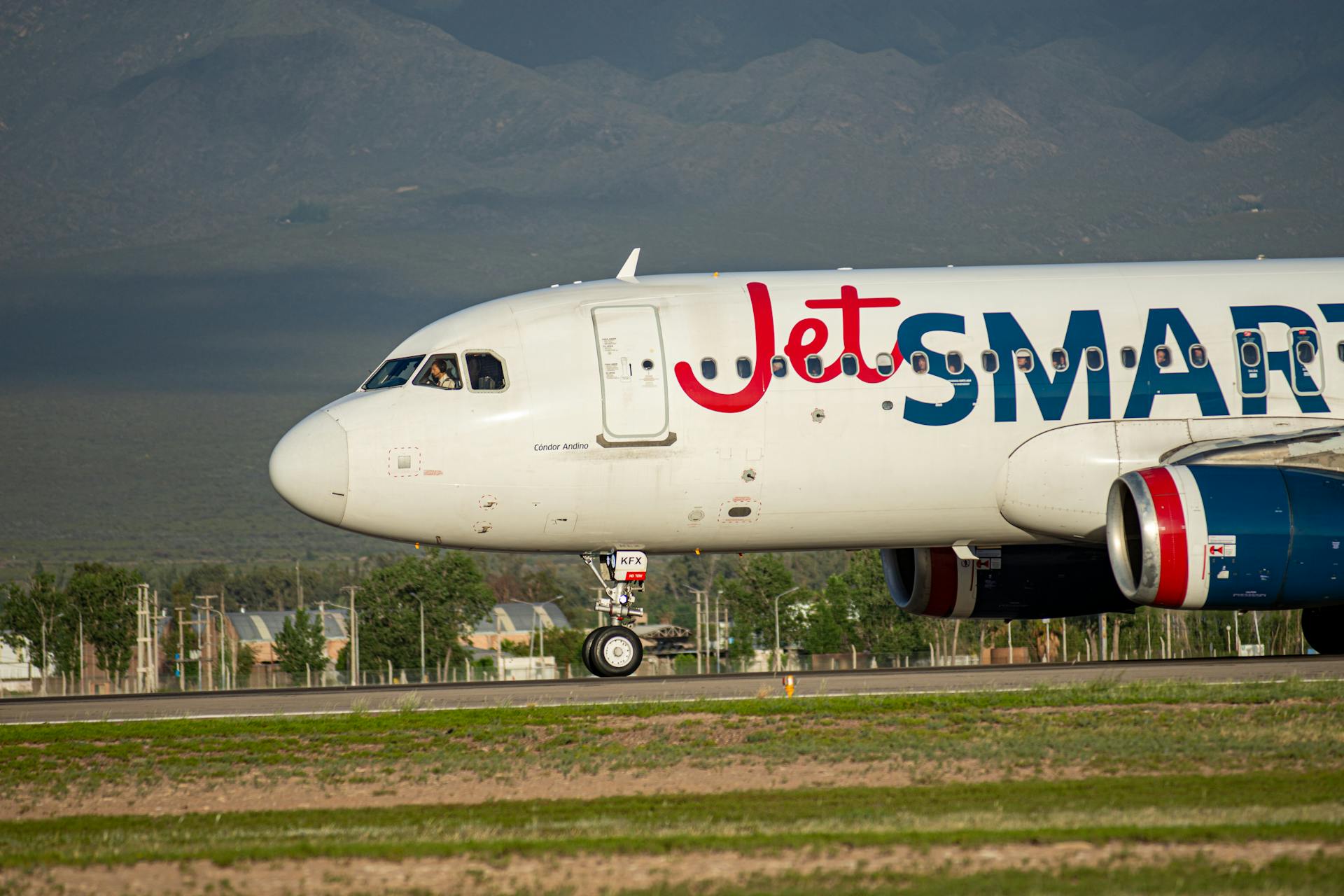 A JetSMART airplane taxiing on an airport runway with mountains in the background.