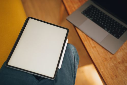 Free A digital tablet on a lap next to a laptop on a wooden table, ideal for work or study. Stock Photo