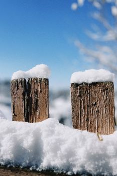 A close-up of snow-covered wooden fence posts against a bright blue sky in Talgar, Kazakhstan.